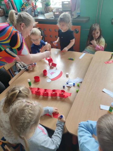 Pani Magdalena z dziećmi kleją elementy z papieru.